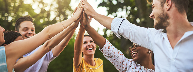 Mehrere Personen stehen im Grünen im Kreis; ihre Hände berühren sich in der Mitte.