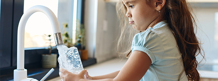 Ein Mädchen füllt sein Glas am Wasserhahn in einer Küche.