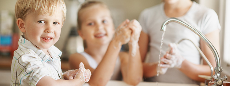 Drei kleine Kinder an einem laufenden Wasserhahn seifen sich die Hände ein.