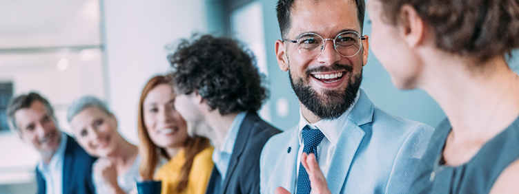 Mehrere Personen sitzen nebeneinander in einem Büroraum und unterhalten sich.