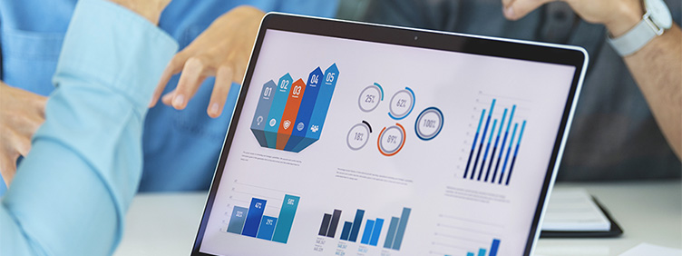 Ein Bildschirm mit Grafiken steht auf einem Tisch. Dahinter sind gestikuliernde Hände zu sehen.