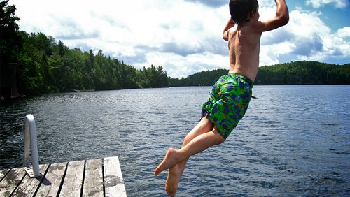 Ein Junge in Badehose sprint von einem Holzanleger in einen See.