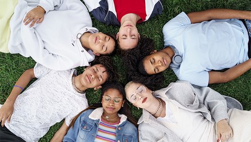 Jugendliche liegen sternförmig mit ihren Köpfen in der Mitte auf einer Wiese.
