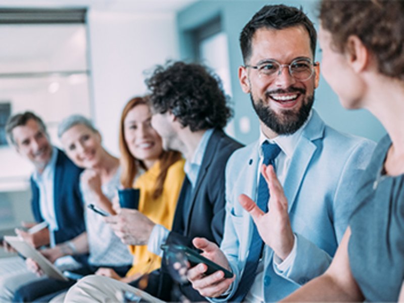 Mehrere Personen sitzen nebeneinander in einem Büroraum und unterhalten sich.