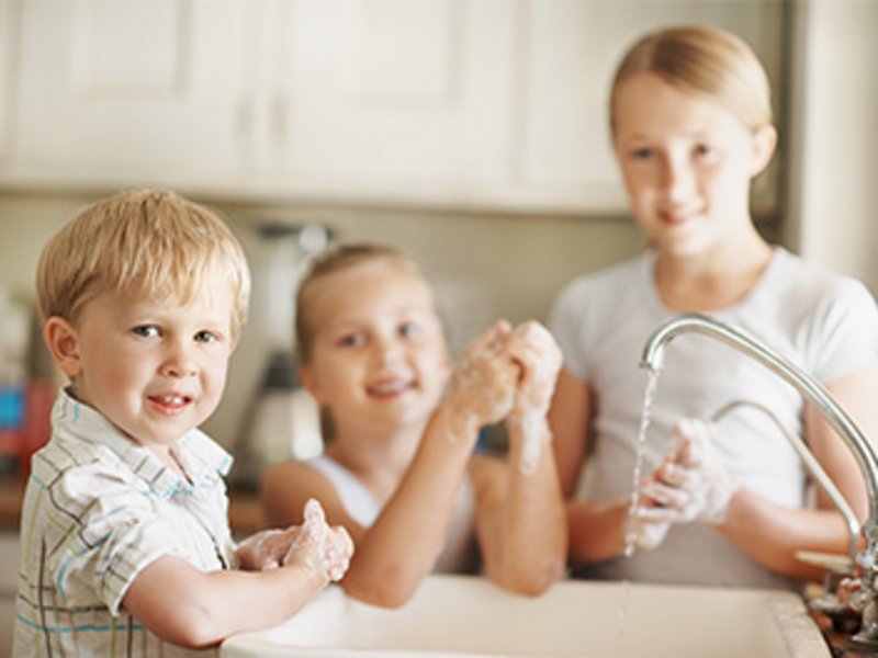 Drei kleine Kinder an einem laufenden Wasserhahn seifen sich die Hände ein.