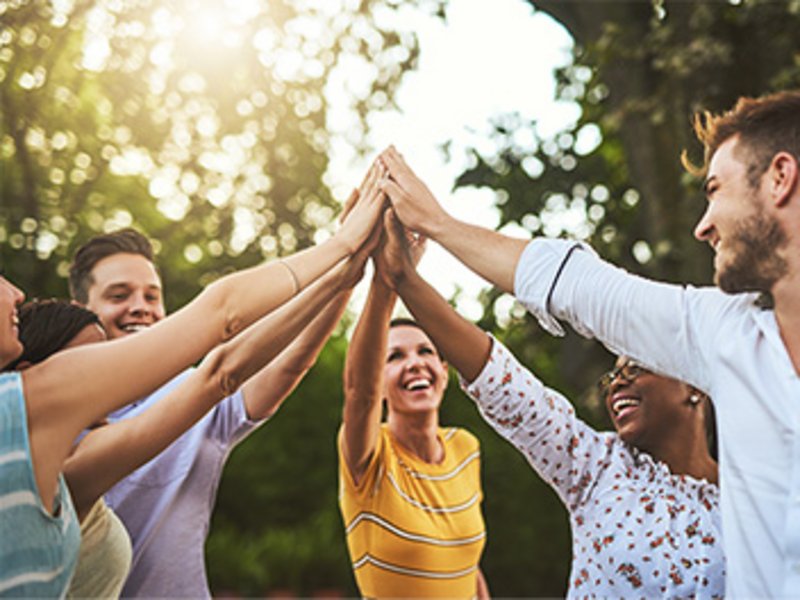 Mehrere Personen stehen im Grünen im Kreis; ihre Hände berühren sich in der Mitte.