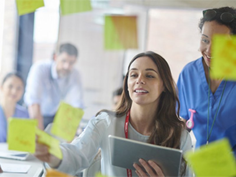 Mehrere Personen in einem Büroraum machen ein Brainstorming mit Hilfe von Notizzetteln.
